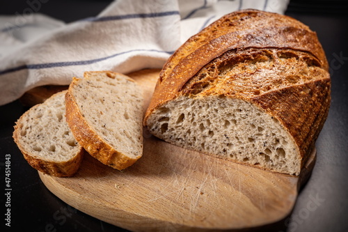  Fresh baked Sliced Fermented Sourdough Buckwheat Bread on wooden cutting board on blackboard Side View With Slices and kitchen towel