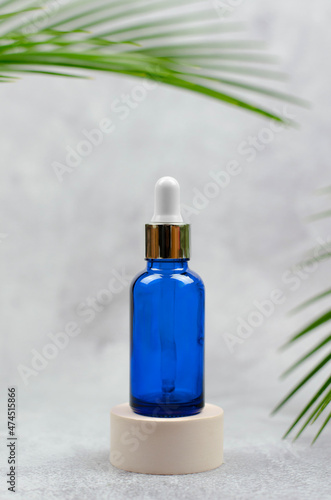 Turquoise cosmetic bottle with dropper on beige podium with palm leaves. Skin Care Cosmetics