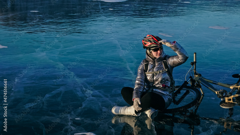 Woman sitting near her bike on ice. The girl cyclist stopped to Woman sitting near her bike on ice. The girl cyclist stopped to