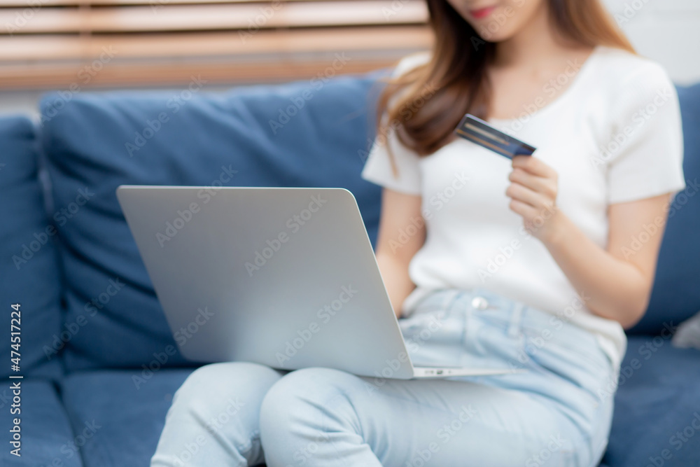 Naklejka premium Young asian woman sit on sofa using laptop computer shopping online with credit card buying to internet, happy girl payment with e-business on couch, purchase and payment, business concept.