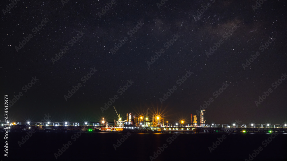 Oil ship tanker loading oil at the oil brige on the sea from refinery for transportation. at night over lighting and starlight background process