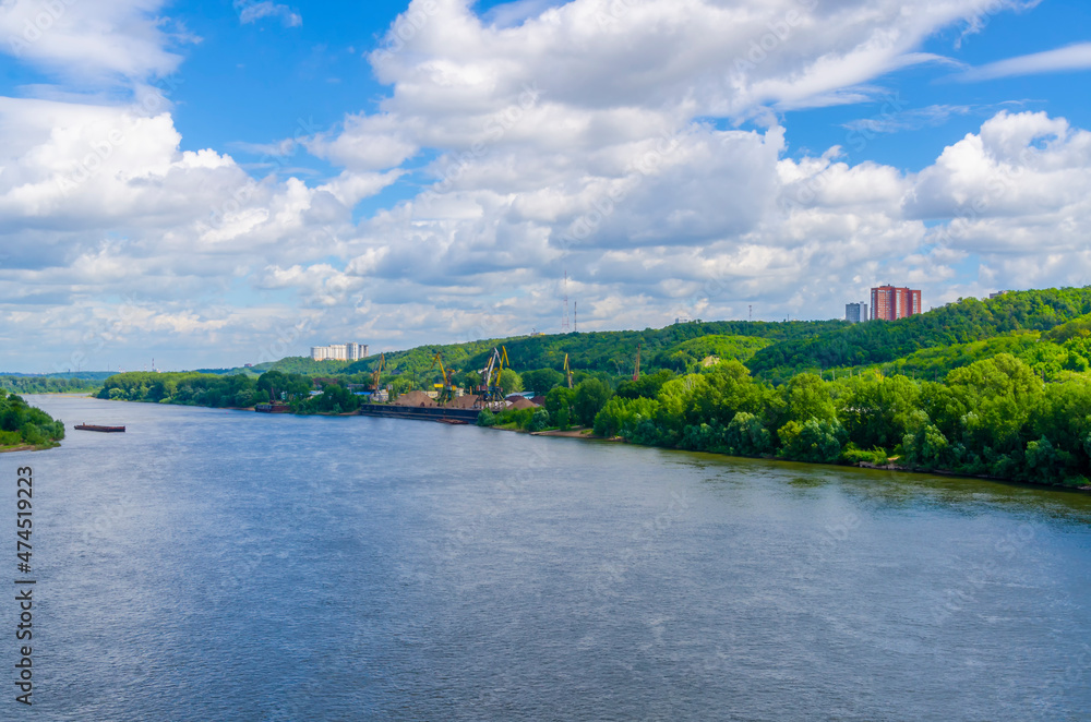 Summer landscape with river, green hill and warm blue cloudy sky. There is a small port on the shore with loading cranes. Summer landscape with river, green hill and warm blue cloudy sky. There is a small port on the shore with loading cranes.