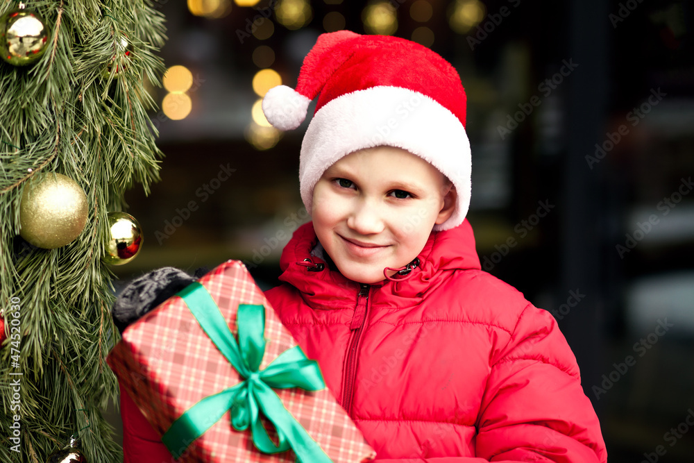 Boy kid in winter clothes standing outside near by shop market, holding gift box. Christmas and New Year shopping concept. Boy kid in winter clothes standing outside near by shop market, holding gift box. Christmas and New Year shopping concept.