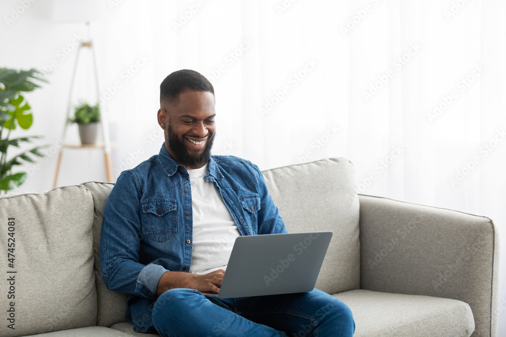 Smiling millennial african american bearded man typing on laptop, watching online video, working and surfing in internet