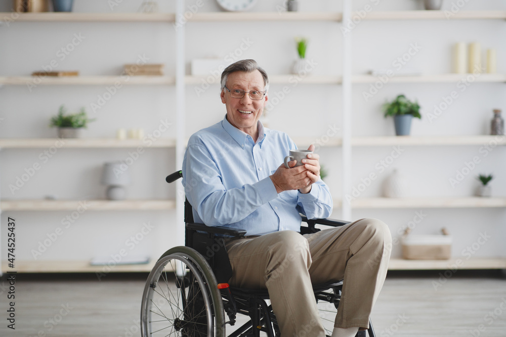 Positive senior man with disability sitting in wheelchair, drinking coffee or tea at home Positive senior man with disability sitting in wheelchair, drinking coffee or tea at home