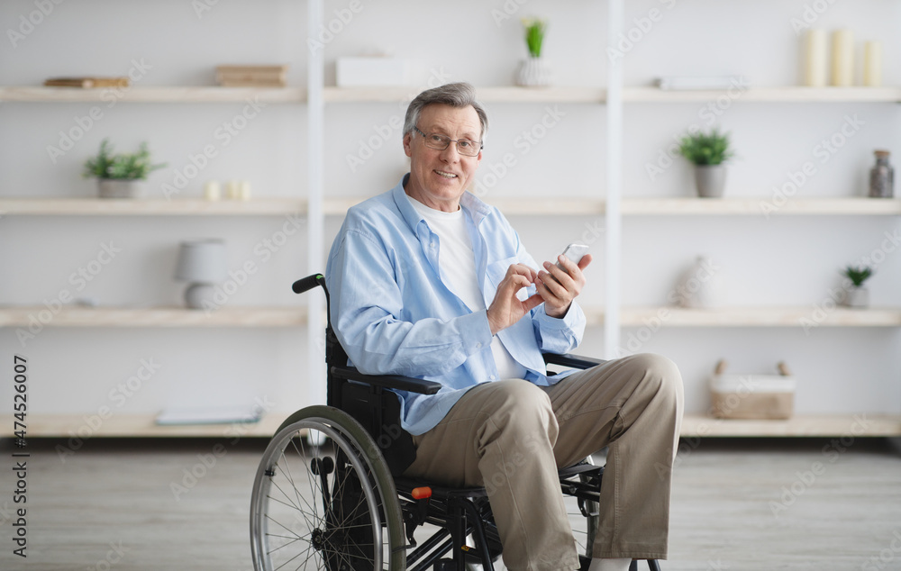 Positive senior man in wheelchair makin video call or browsing web on smartphone at home Positive senior man in wheelchair makin video call or browsing web on smartphone at home