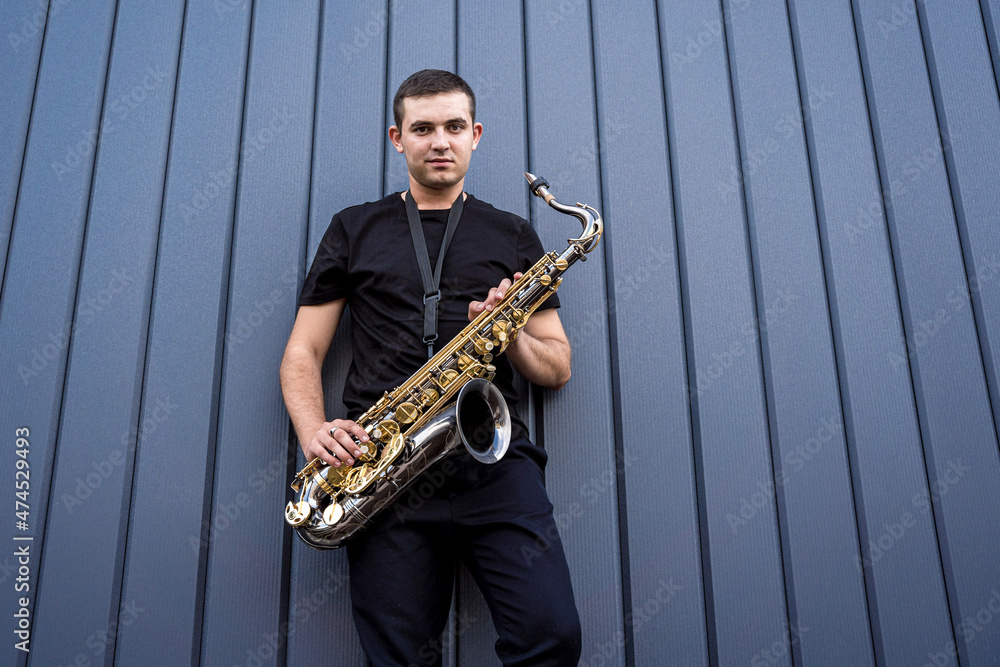 Naklejka premium Young street musician playing saxophone near the big blue wall