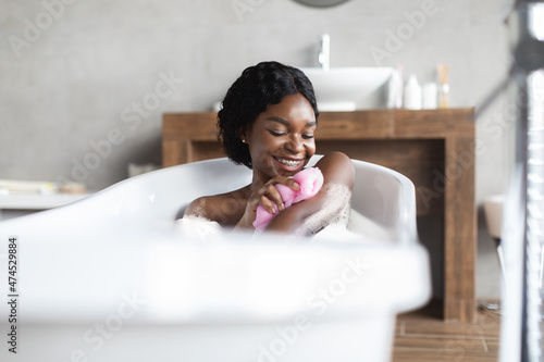 Happy young black lady taking foamy bath  exfoliating skin