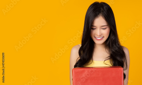 Happy smiling young asian woman holding red gift box and get happy when she receive red gift box Look at the box Stand over yellow background Beautiful Asia girl happy smile hold birthday present box 