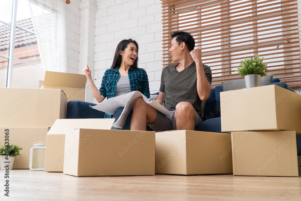 Smiling young Asian happy couple hold blueprint for home decoration ideas at moving day in their new home after buying real estate. Concept of starting a new life for a newly married couple. Smiling young Asian happy couple hold blueprint for home decoration ideas at moving day in their new home after buying real estate. Concept of starting a new life for a newly married couple.