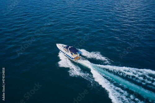 White boat with blue awning moves in the sea aerial view. Large white yacht movement on the water diagonally top view. © Berg