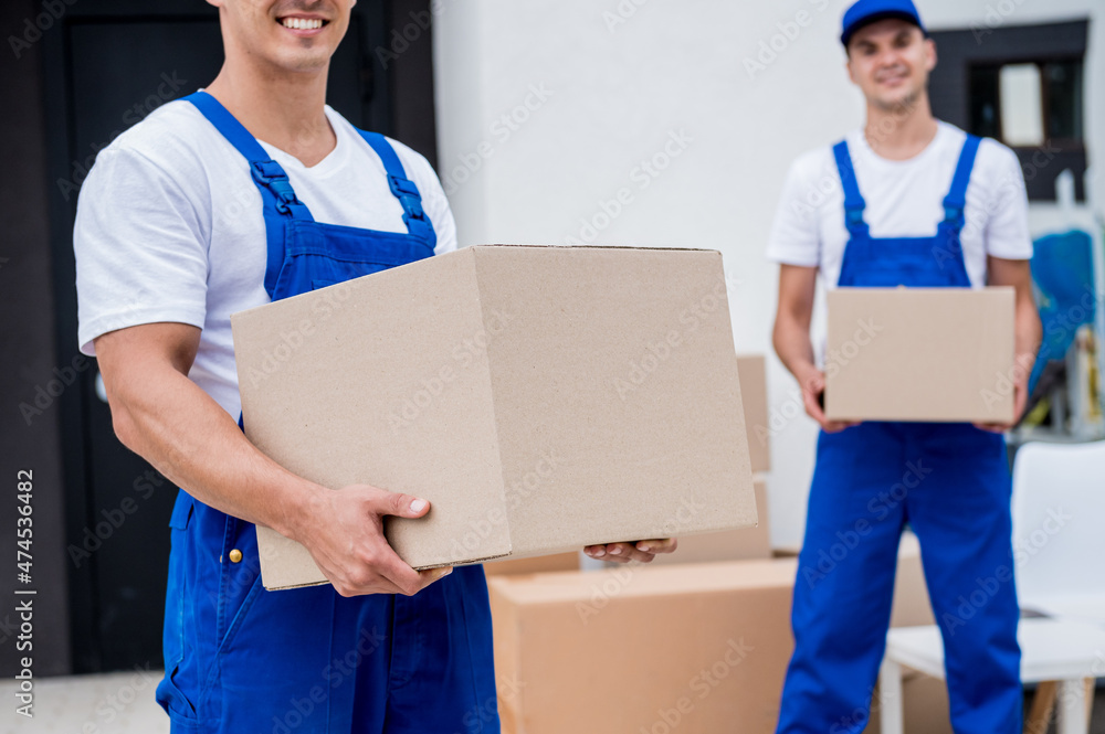 Two removal company workers are loading boxes into a minibus. Two removal company workers are loading boxes into a minibus.