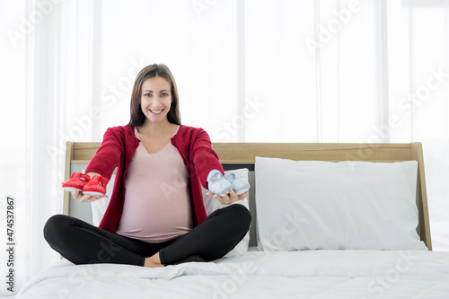 New moms, Europeans, Russians, are pregnant. Choose between red and blue shoes for your upcoming baby, happily and smilingly in the bedroom.