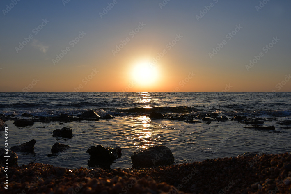 Sunrise over the sea. Small waves run into the stony coast. Solar path on the water