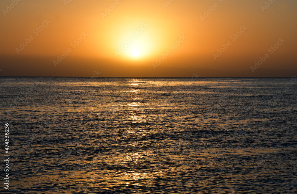 Sunrise over the sea. The bright yellow-gold color of the sky. The glare of the sun and a slight swell on the surface of the water