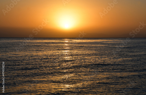 Sunrise over the sea. The bright yellow-gold color of the sky. The glare of the sun and a slight swell on the surface of the water