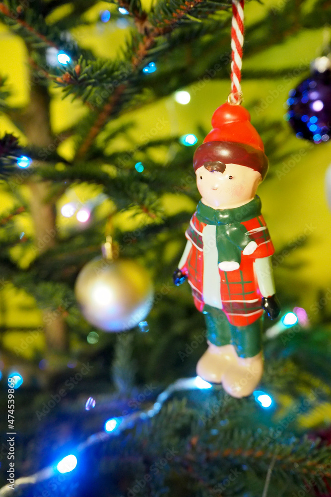 Obraz premium a wooden toy boy is hanging on a Christmas tree with glowing garlands. side view