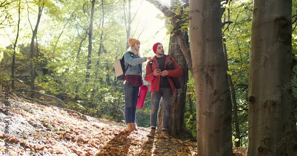 Close up of young man holding smartphone. Couple with backpacks using map at the special app and pointing in direction during adventure trek in wood. Concept of people traveling in nature Close up of young man holding smartphone. Couple with backpacks using map at the special app and pointing in direction during adventure trek in wood. Concept of people traveling in nature