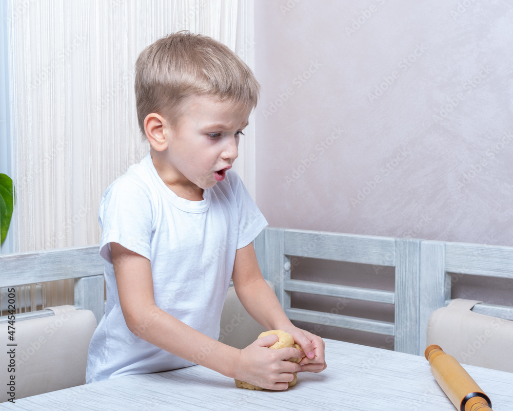 Fototapeta premium Cooking traditional gingerbread. Emotional boy kneads raw dough to make cookies. Child helps mom with Christmas cooking