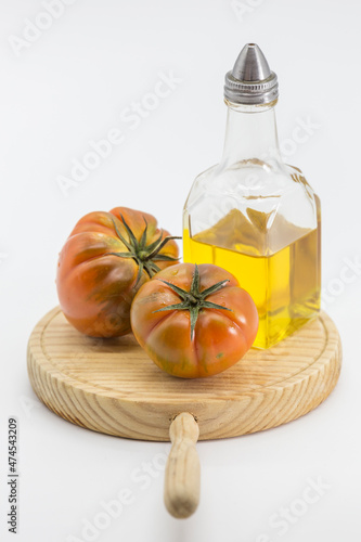 two tomatoes and an oil can on a wooden board