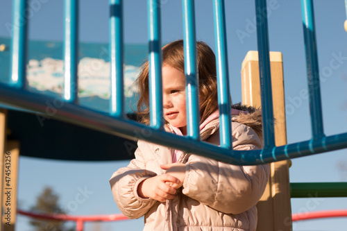 Small child with long red hair against the background of a blue sky in warm clothes on the playground