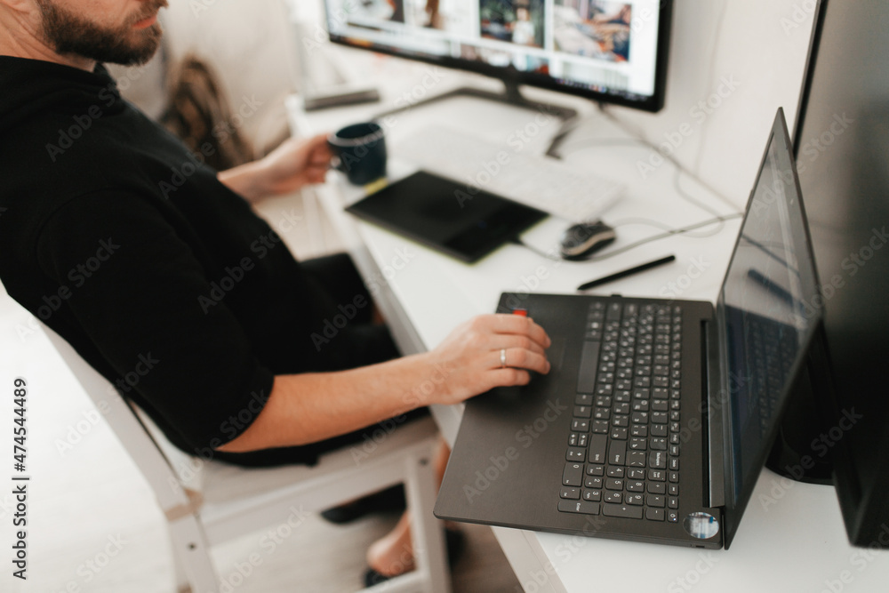 Millennial man working from home on computer and laptop Millennial man working from home on computer and laptop