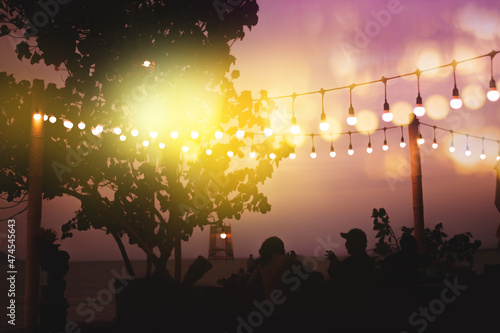 blurred bokeh light on sunset with yellow string lights decor in beach restaurant