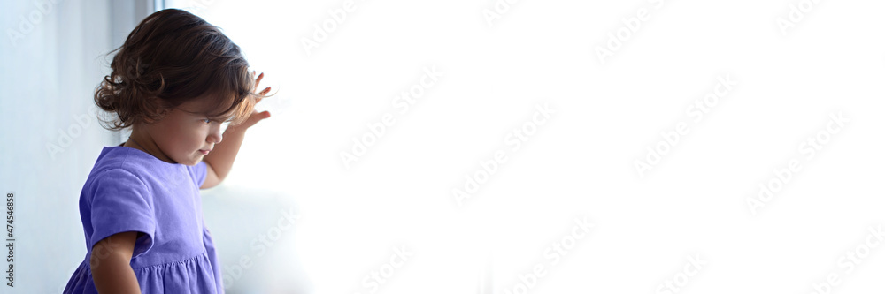 Little girl looks out the window and touches the glass with her fingers. Web banner. Little girl looks out the window and touches the glass with her fingers. Web banner.