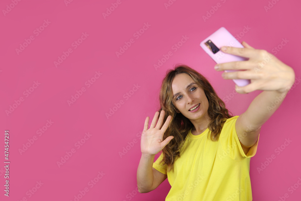 Smiling young girl takes selfie photo onsmartphone on pink background. Copy space for text Smiling young girl takes selfie photo onsmartphone on pink background. Copy space for text