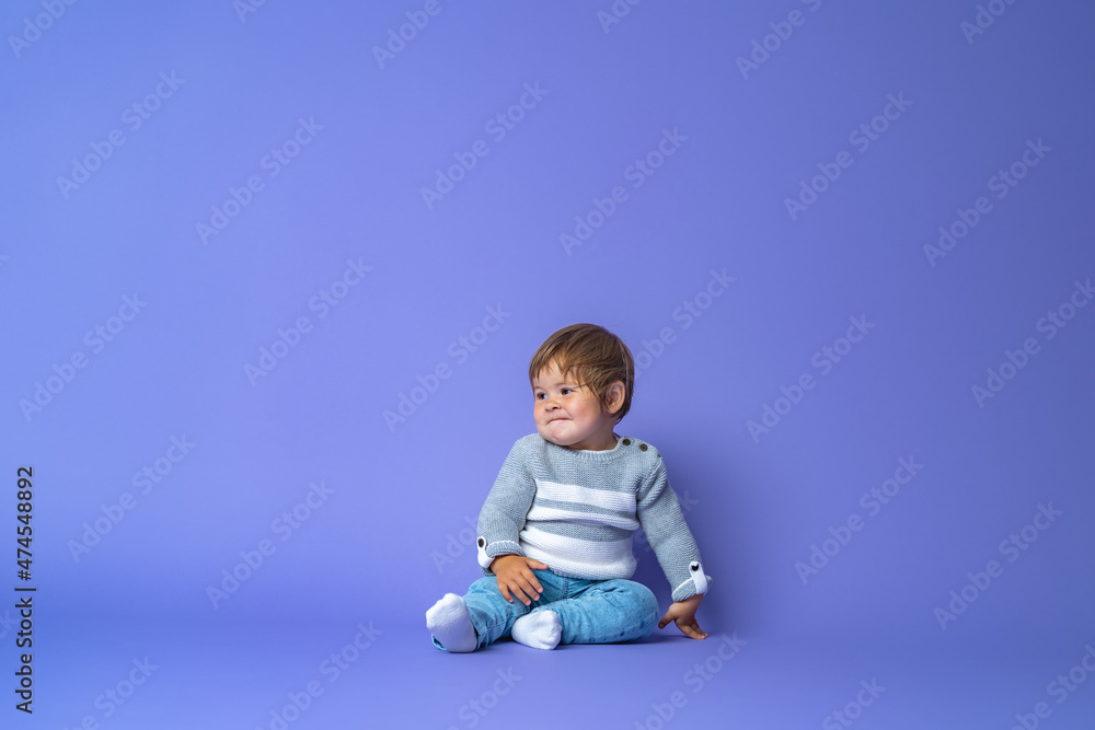 a one-year-old baby girl is sitting on a blue background in warm knitted clothes. free space for text and copy space