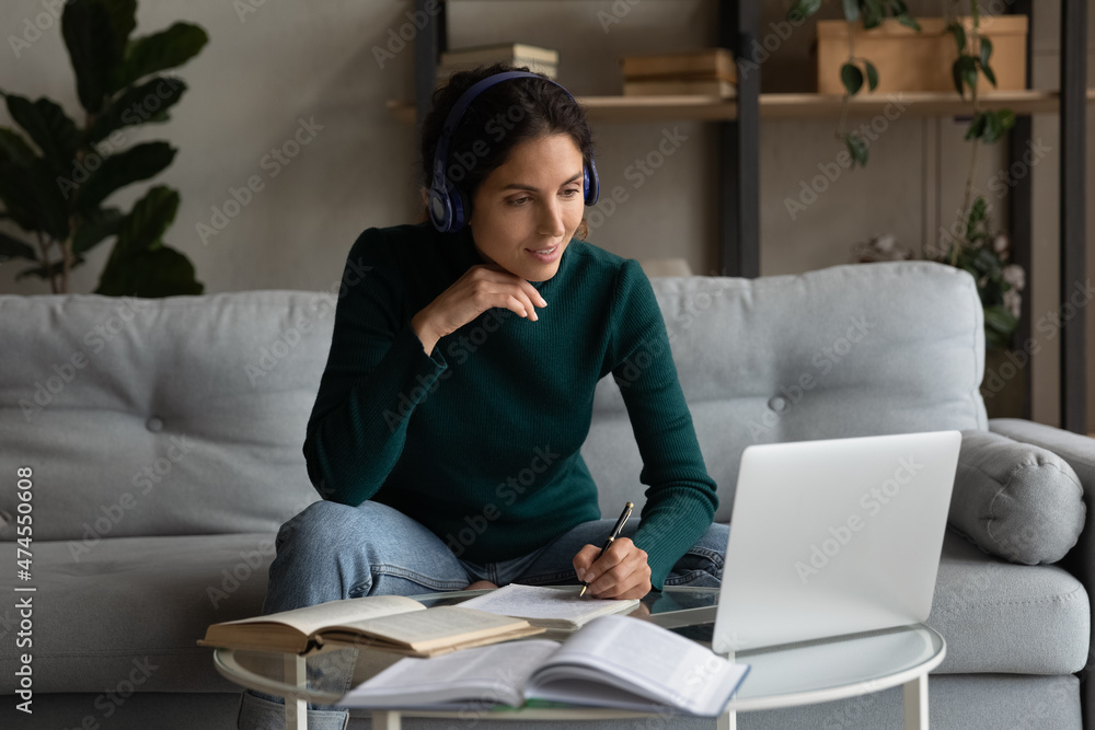 Millennial Latino woman in headphones make note write studying online on laptop at home. Young Hispanic female student busy working on internet on computer, take distant course. Education concept. Millennial Latino woman in headphones make note write studying online on laptop at home. Young Hispanic female student busy working on internet on computer, take distant course. Education concept.