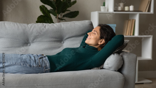 Happy calm young Latino woman lying on couch in living room relax sleeping or taking nap. Peaceful asleep millennial hispanic female rest on sofa at home breathe fresh air relieve negative emotions.