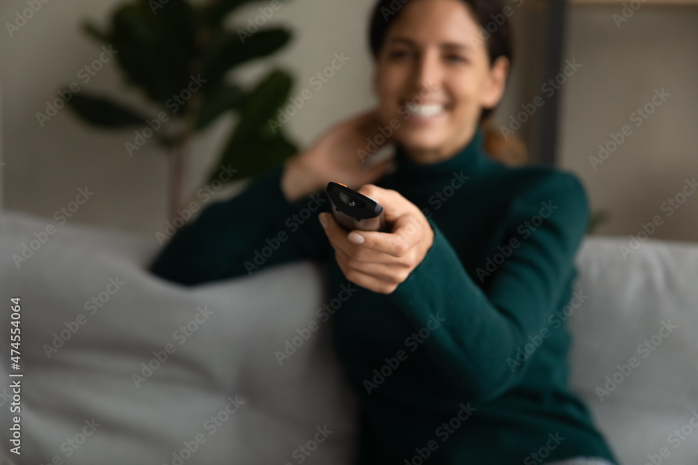 Fototapeta premium Crop close up of smiling Hispanic woman relax at home watch TV switch channel with remote control. Happy Latin female rest have fun enjoy television program online. Technology, entertainment concept.