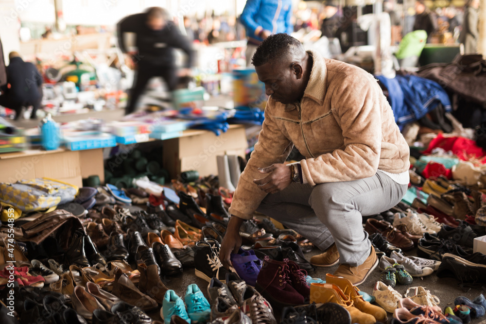 Obraz premium Afro-American guy considers sacond hands shoes on flea market