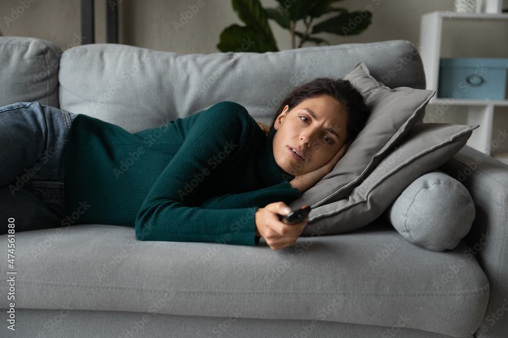 Calm young Hispanic woman lying relaxing on couch in living room watch TV switch channels with remote controller. Millennial latin female rest on sofa at home enjoy television. Entertainment concept. Calm young Hispanic woman lying relaxing on couch in living room watch TV switch channels with remote controller. Millennial latin female rest on sofa at home enjoy television. Entertainment concept.