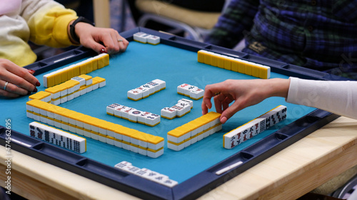 A mahjong table with an active game and the hands of the participants in the game. An ancient Asian game called Mahjong as a way to relax and have fun.