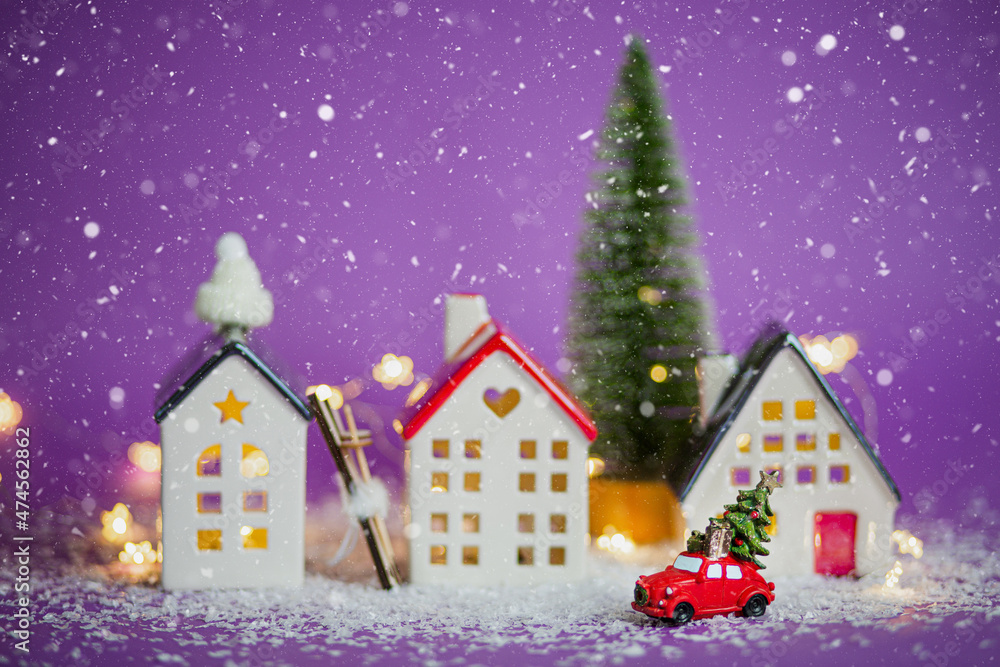 Christmas decor - red retro car on snow carries past houses with fairy lights in bokeh Christmas tree with gift boxes on roof. Toy on violet background. New Year greeting card. Cozy home