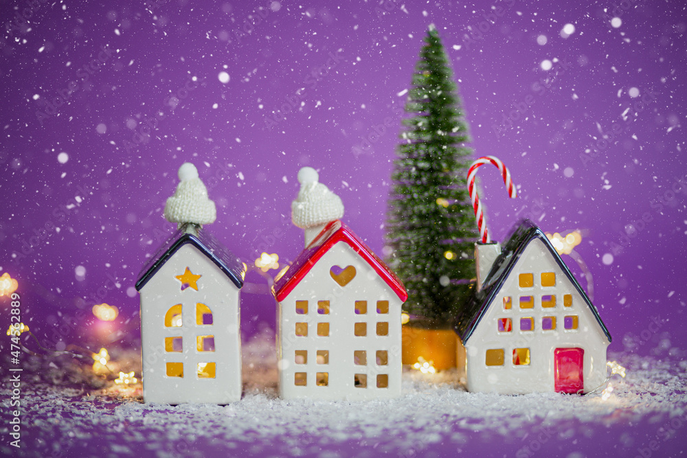 Cozy houses and Christmas tree in snowstorm on violet background and fairy lights. Winter, snow - home insulation, protection from cold and bad weather. Festive mood, Christmas, New Year greeting card