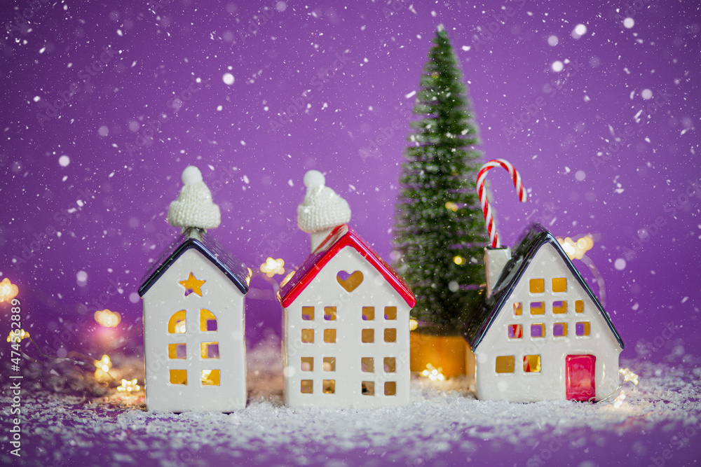 Cozy houses and Christmas tree in snowstorm on violet background and fairy lights. Winter, snow - home insulation, protection from cold and bad weather. Festive mood, Christmas, New Year greeting card Cozy houses and Christmas tree in snowstorm on violet background and fairy lights. Winter, snow - home insulation, protection from cold and bad weather. Festive mood, Christmas, New Year greeting card