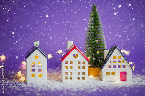 Cozy houses and Christmas tree in snowstorm on violet background and fairy lights. Winter  snow - home insulation  protection from cold and bad weather. Festive mood  Christmas  New Year greeting card