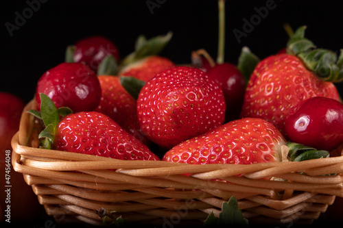 Basket with strawberries and cherries. Black background.