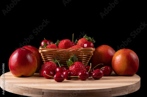 Basket with strawberries and cherries and nectarines. Bamboo board. black background. Space for text.