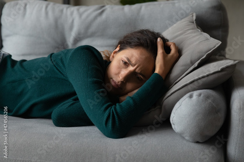 Upset millennial Latino woman lying on couch at home feel depressed with life problems troubles. Unhappy young Hispanic female rest on sofa distressed with abortion or miscarriage. Drama concept.