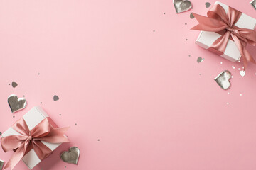 Top view photo of white gift boxes with pink bows silver decorative hearts sequins and heart shaped confetti on isolated pastel pink background with empty space
