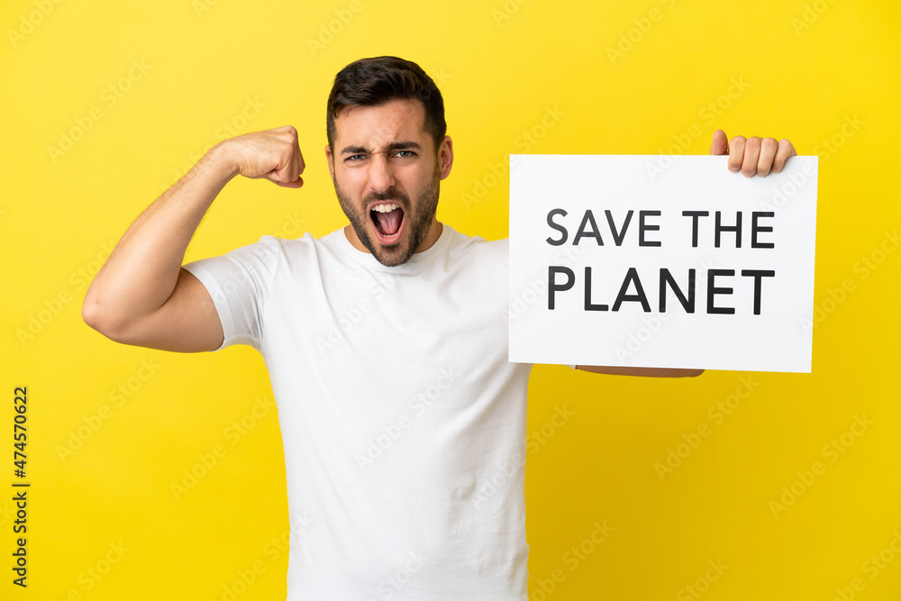 Young handsome caucasian man isolated on yellow background holding a placard with text Save the Planet and doing strong gesture Young handsome caucasian man isolated on yellow background holding a placard with text Save the Planet and doing strong gesture