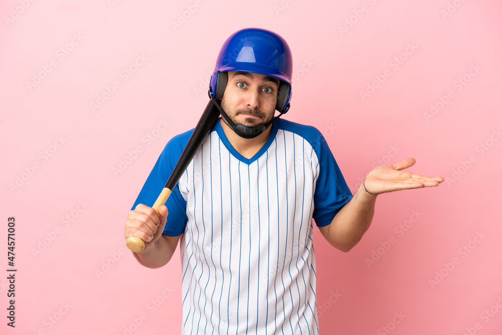 Baseball player with helmet and bat isolated on pink background having doubts while raising hands Baseball player with helmet and bat isolated on pink background having doubts while raising hands