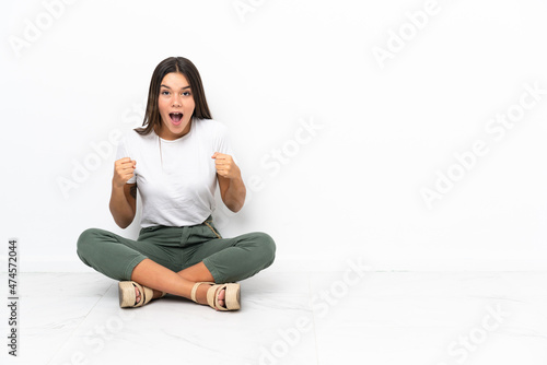 Teenager girl sitting on the floor celebrating a victory in winner position