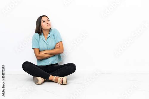 Teenager girl sitting on the floor making doubts gesture while lifting the shoulders