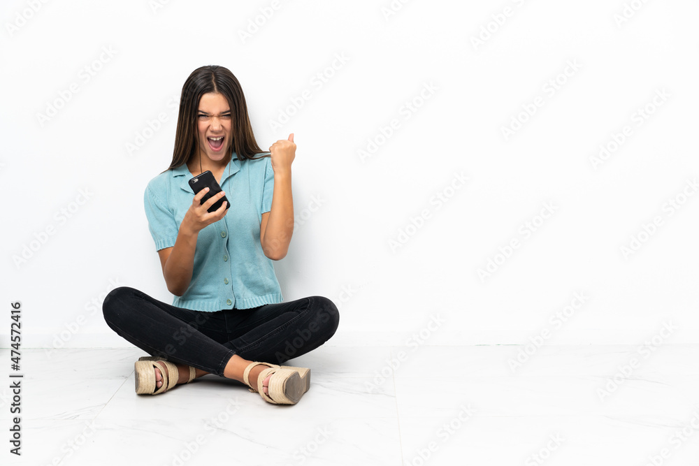 Teenager girl sitting on the floor with phone in victory position Teenager girl sitting on the floor with phone in victory position