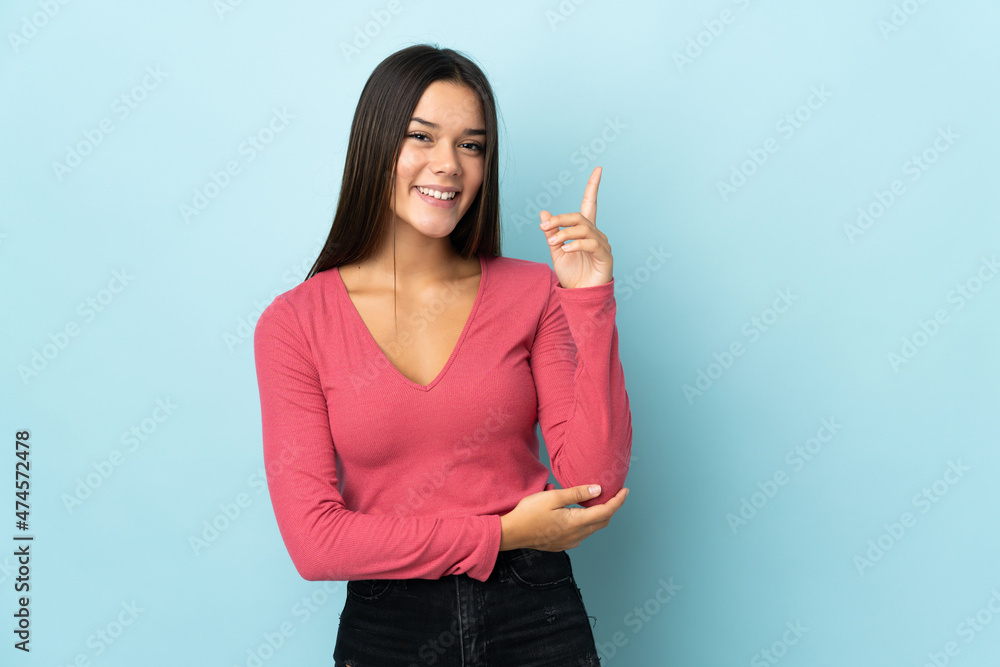 Teenager girl isolated on blue background happy and pointing up Teenager girl isolated on blue background happy and pointing up